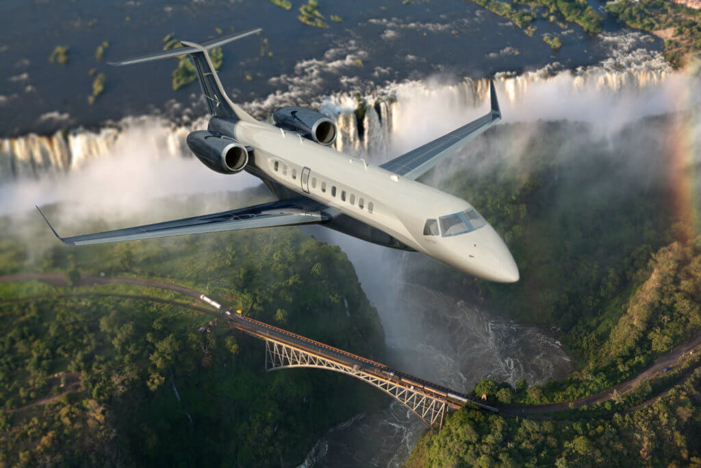 Embraer Legacy 650E flying with bridge and greenery in background.