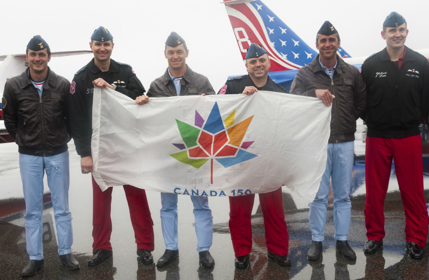 Members of the Canadian Forces Snowbirds and La Patrouille de France hold an autographed Canada 150 flag.