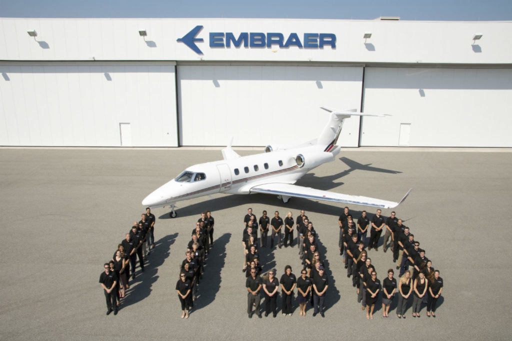 Embraer employees stand in front of the 1,100th business jet the company has delivered, a Phenom 300