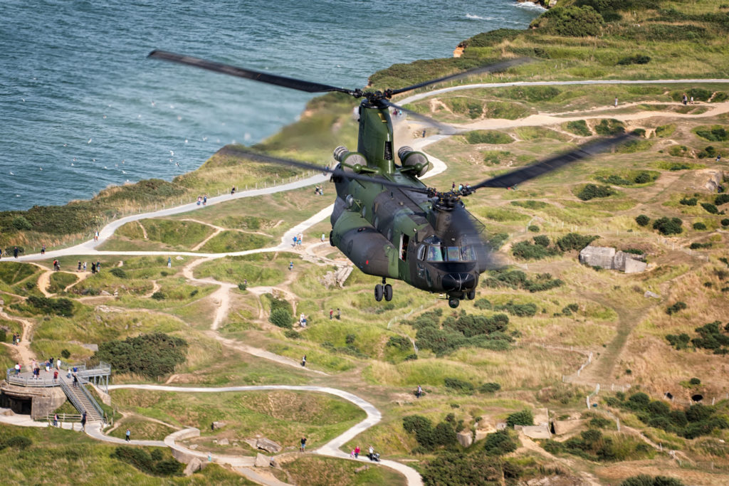 The RCAF CH-147F Chinook flies over the English countryside as observers walk on winding paths below.