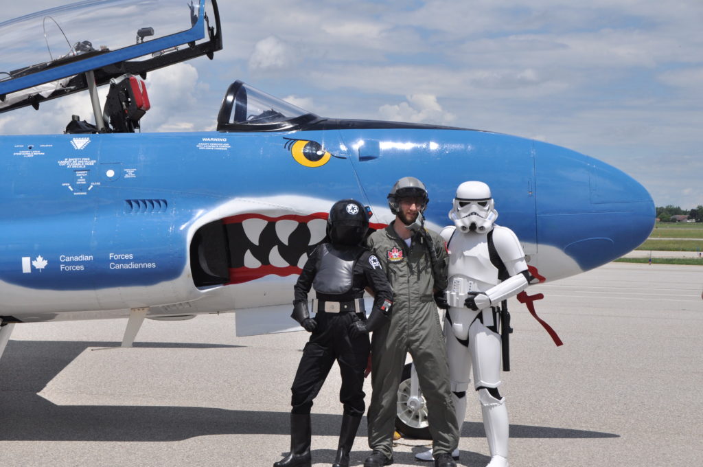 Pilot, stormtrooper and one other character stand with aircraft