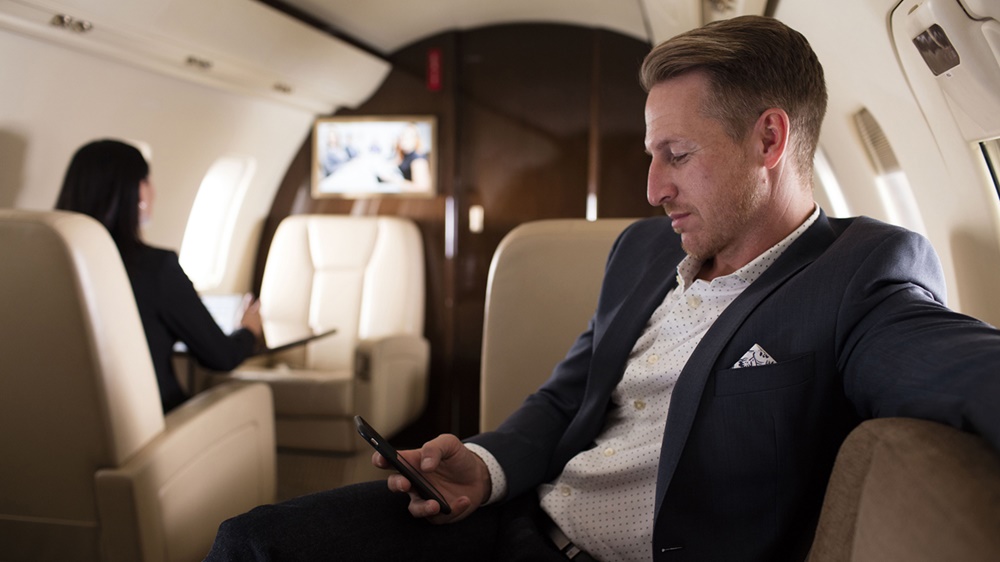 Man checks his cell phone while sitting in business jet cabin.