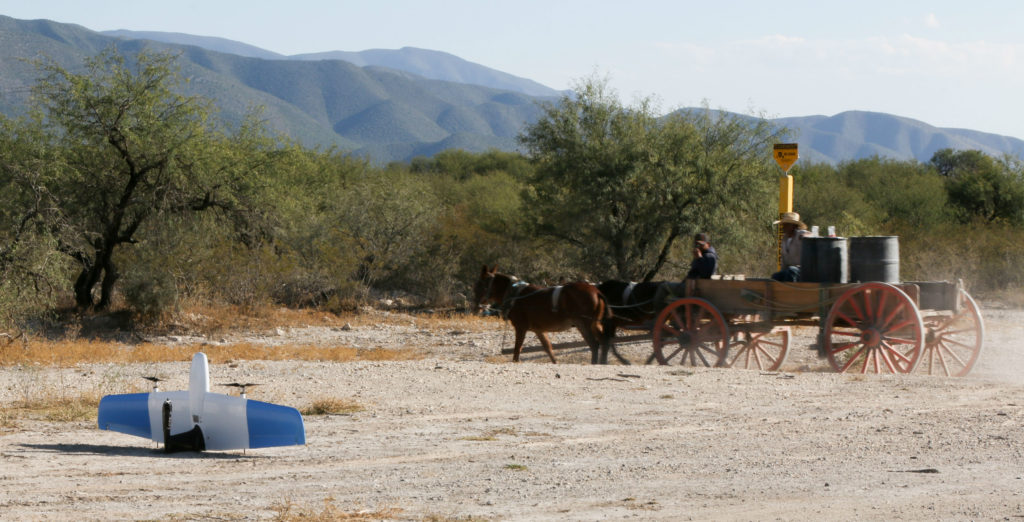 The SkyOne drone rests on the ground in rural Mexico, while two men pass by on a horse-drawn buggy.