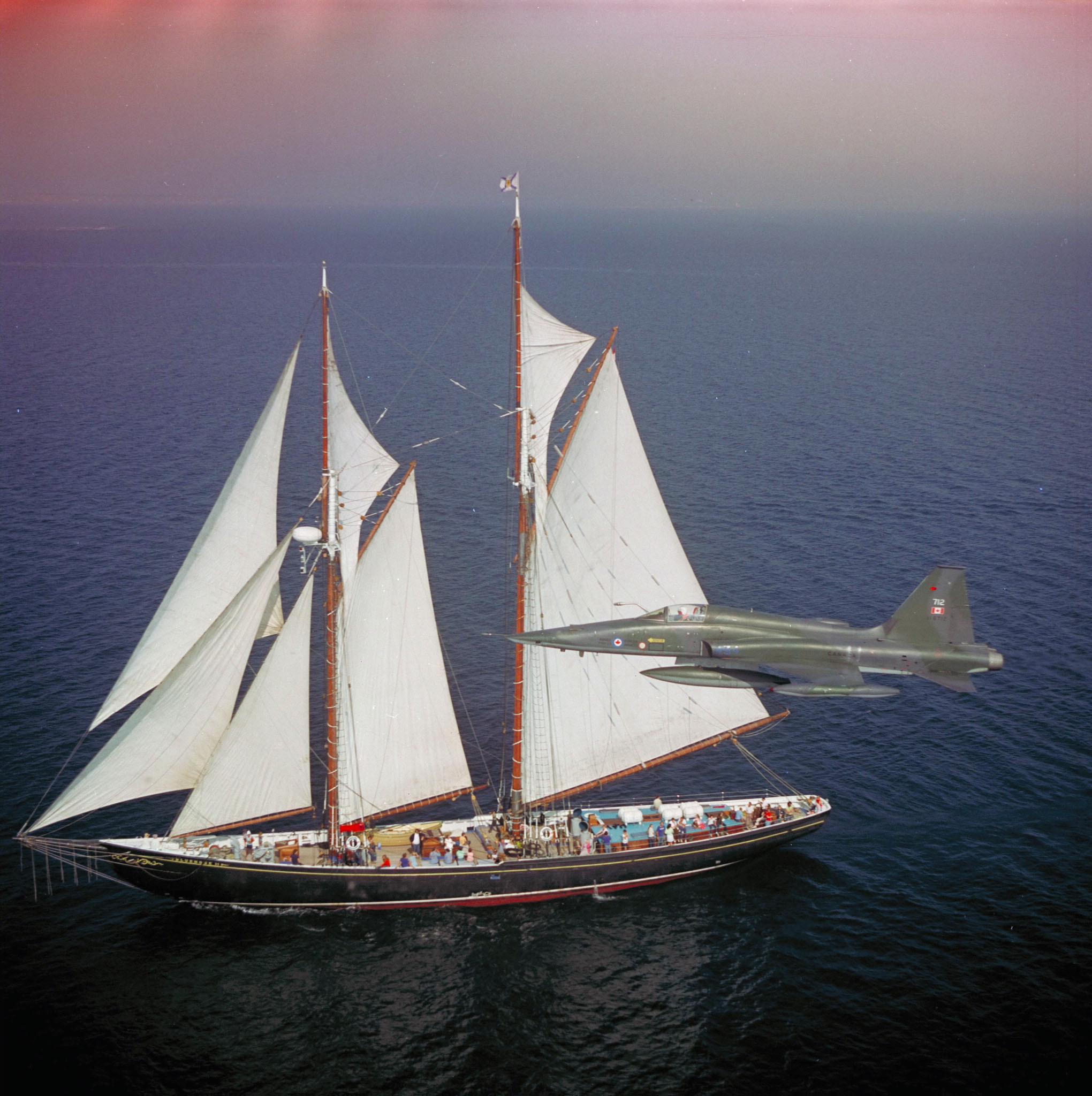 An F-5 aircraft (officially designated as the CF-116 Freedom Fighter) from 434 “Bluenose” Squadron flies over the Bluenose II in a circa 1975 photo. DND Photo
