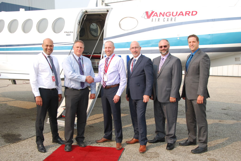Several men stand in front of a Vanguard Air Care aircraft.
