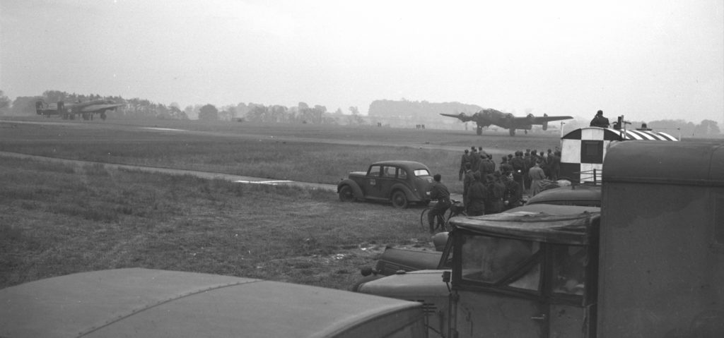 A Bluenose squadron Halifax of RCAF Bomber Group Overseas thunders into the air on its way to help crush German defences in France. Ground crew officers and men gather to watch it. RCAF Photo